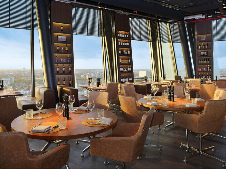 Das clouds Restaurant in Hamburg mit dunklem Ambiente, Ledersesseln, warmer Beleuchtung und runden Holztischen.