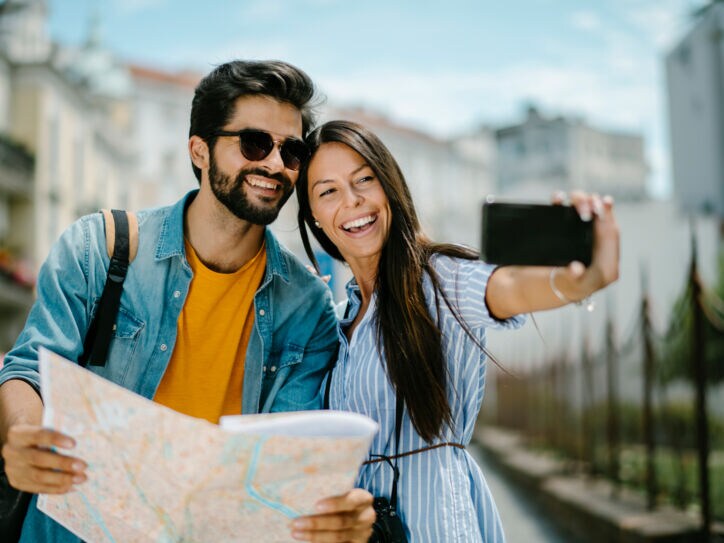 Ein fröhliches Paar mit Straßenplan beim Selfie fotografieren in urbaner Umgebung.