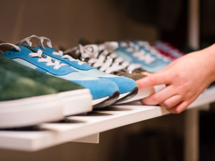 Eine Hand greift nach einem Sneaker aus einer Reihe von Turnschuhen in einem Regal.