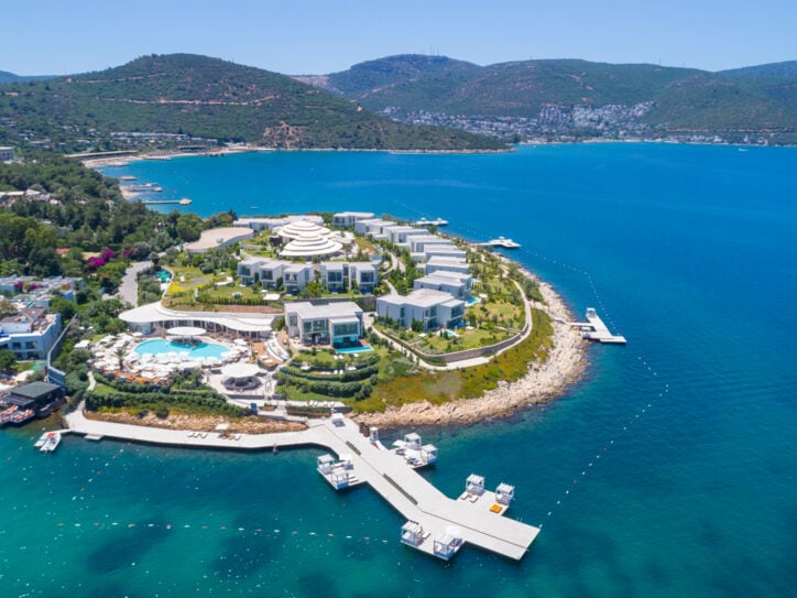 Luftaufnahme eines luxuriösen Hotelresorts mit weißen Bungalows auf einer Landzunge, umgeben von blauem Meer.