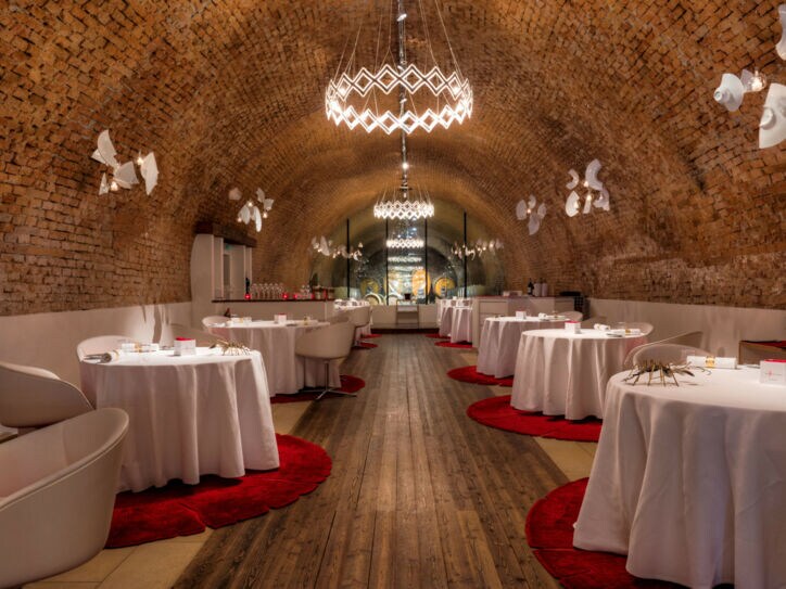 Speisesaal mit weiß eingedeckten, runden Tischen in einem Ziegelgewölbekeller.