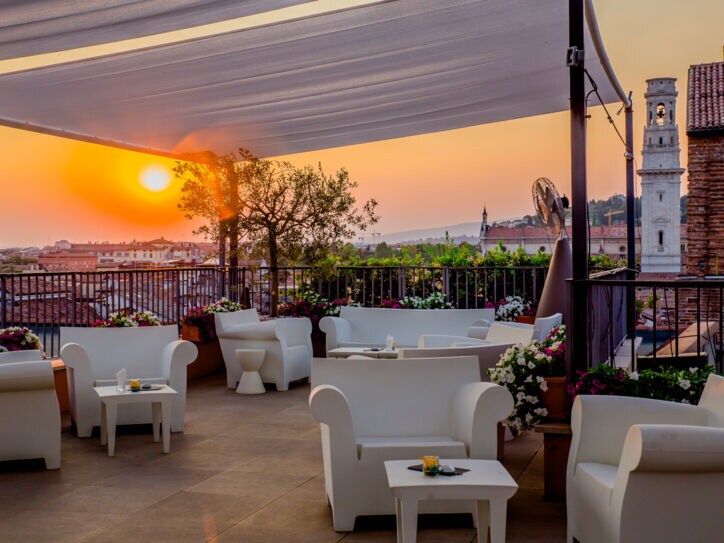 Dachterrasse mit weißen Sitzmöbeln in urbaner, mediterraner Umgebung bei Sonnenuntergang.