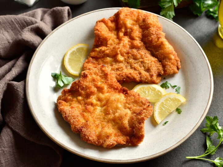 Ein Wiener Schnitzel auf einem Teller mit Zitronenscheiben.
