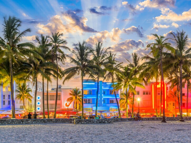 Strandpromenade mit Palmen und Art-déco-Gebäuden mit Neon-Beleuchtung am Abend.