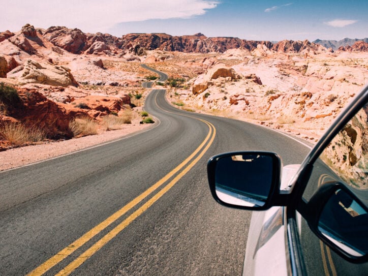 Seitenspiegel eines Autos auf einer US-amerikanischen Autobahn in einer felsigen Wüstenlandschaft.