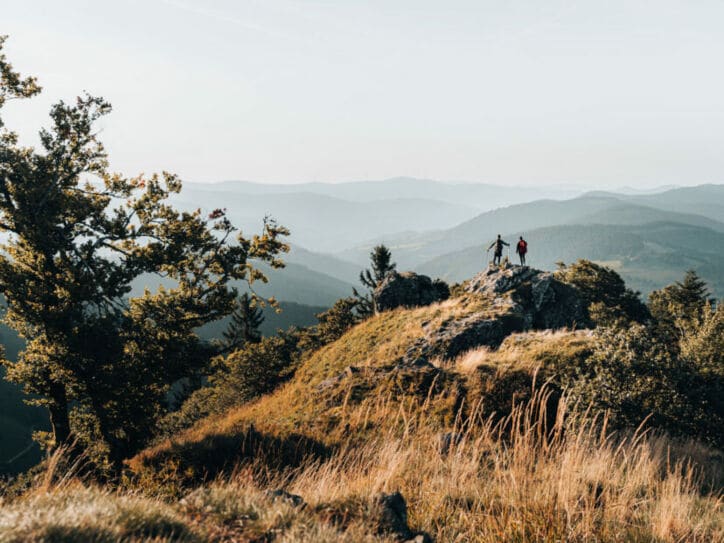 Zwei Personen stehen auf einem Felsen und blicken in die Ferne, im Hintergrund Gipfel im Schwarzwald.