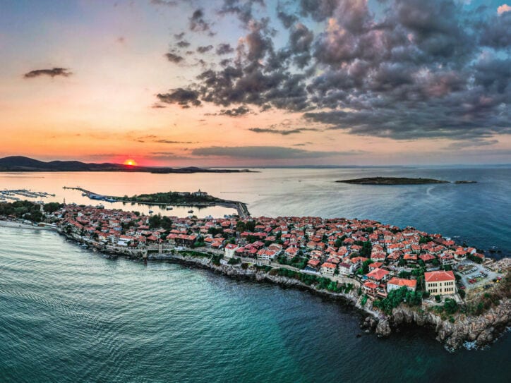 Ortschaft auf einer felsigen Landzunge im Meer unter Wolkenhimmel bei Sonnenuntergang.