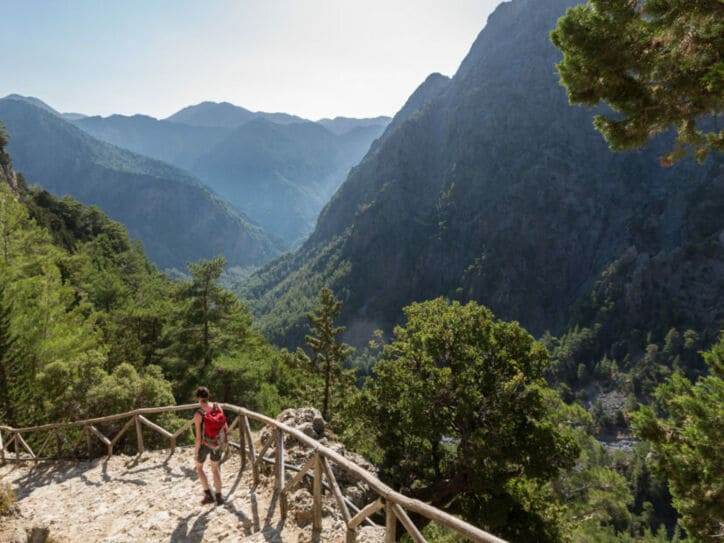 Eine Person beim Wandern in der Samaria-Schlucht auf Kreta, im Hintergrund Vegetation und Berggipfel.