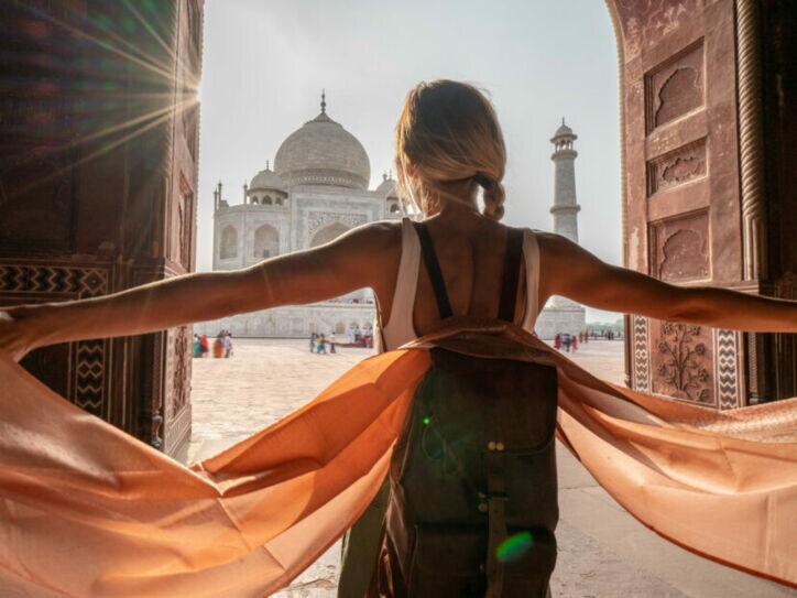 Rückansicht einer Frau mit Rucksack mit ausgestreckten Armen vor dem Taj Mahal.