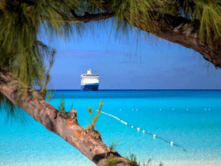 Kreuzfahrtschiff am Horizont eines Karibikstrands mit klarem türkisfarbenem Wasser.