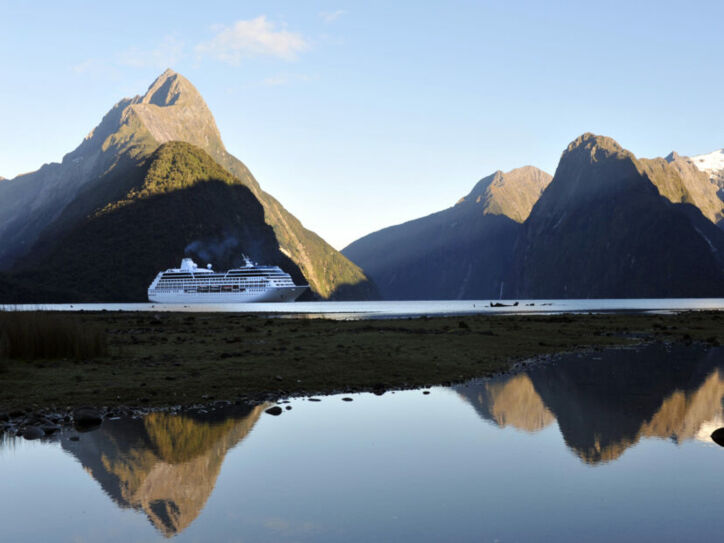 Ein Kreuzfahrtschiff durchquert den Milford Sound in Neuseeland, während sich die hügelige Landschaft des Hintergrunds im ruhigen Wasser spiegelt.