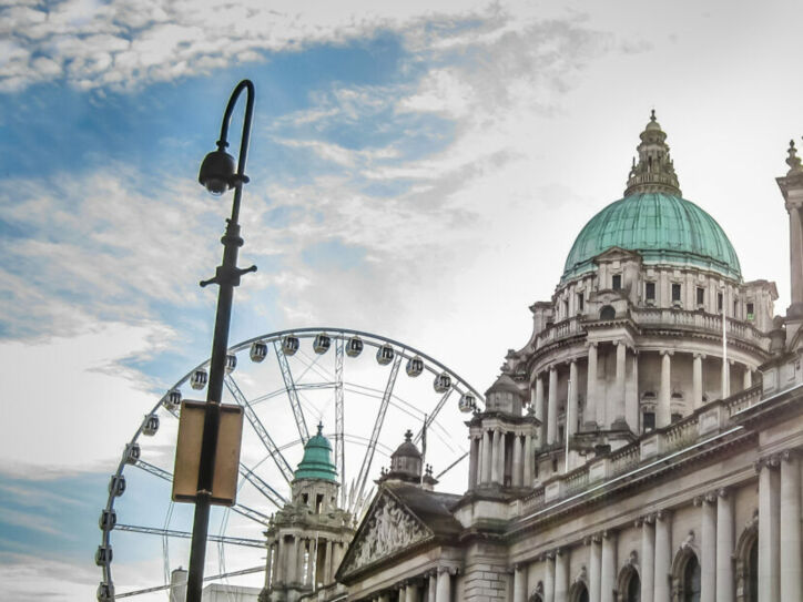 Historisches Gebäude mit grüner Kuppel und Riesenrad im Hintergrund bei Sonnenlicht