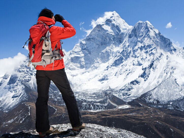 Ein Wanderer in roter Jacke blickt auf einen schneebedeckten Berggipfel im Himalaja
