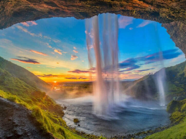 Wasserfall, der von einer Höhle aus bei Sonnenuntergang in eine grüne Landschaft fällt