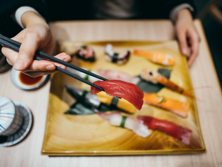 Eine Hand mit Stäbchen über einem Teller mit verschiedenen Sushi-Sorten.
