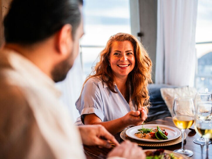 Eine lächelnde Frau im Restaurant sitzt einem Mann gegenüber, zwischen ihnen steht ein hübsch angerichteter Teller.