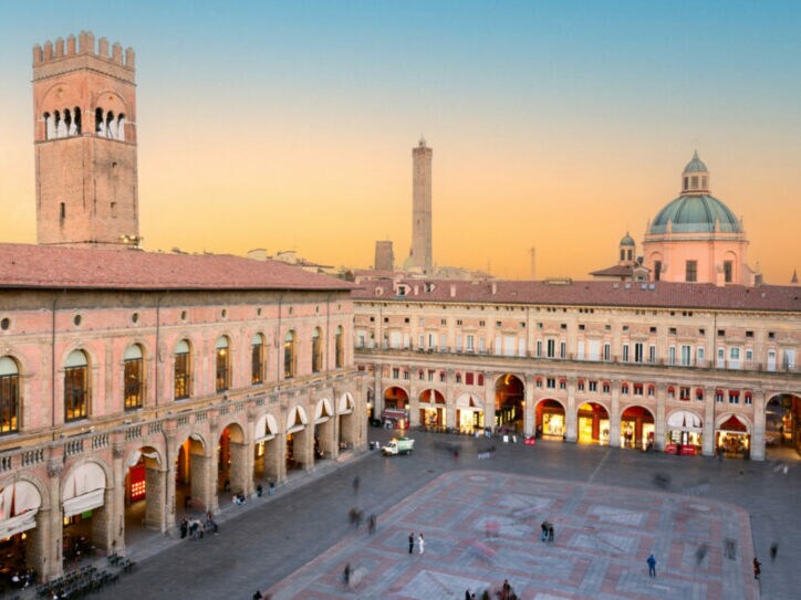 Historische Gebäude mit Arkaden und Turm am Piazza Maggiore in Bologna bei Sonnenuntergang
