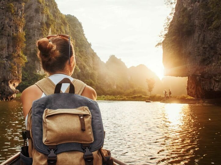 Frau mit Rucksack sitzt in einem Kanu auf einem Fluss, umgeben von hohen Felsen bei Sonnenuntergang.