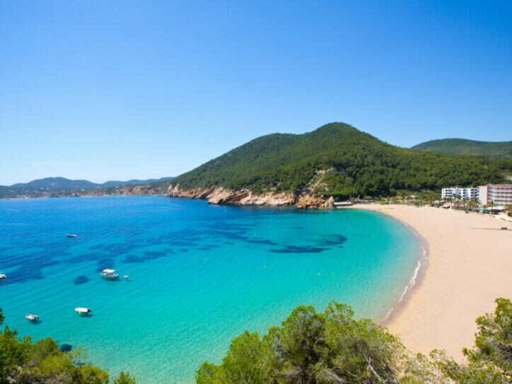 Bucht mit türkisfarbenem Wasser, Sandstrand und bewaldeten Hügeln unter klarem Himmel