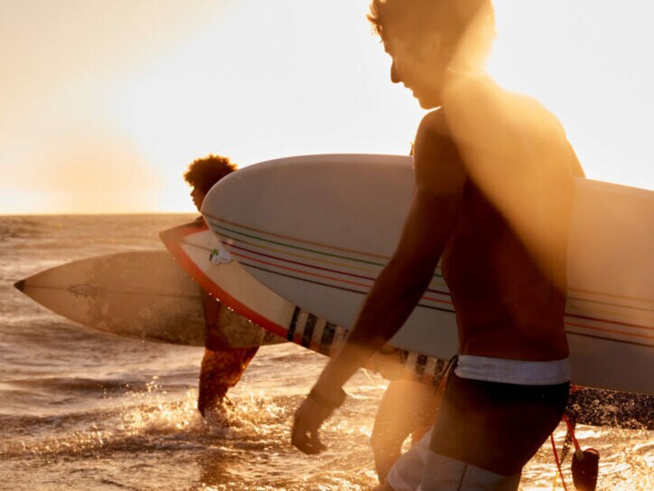 Drei Surfer mit Surfboards laufen bei Sonnenuntergang ins Wasser am Strand