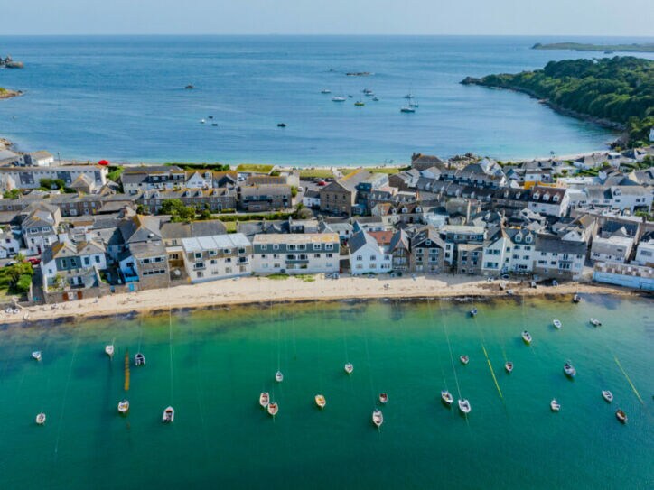 Luftaufnahme eines Küstendorfes mit weißen Häusern, einem Sandstrand und zahlreichen Booten im klaren, grünen Wasser einer Bucht