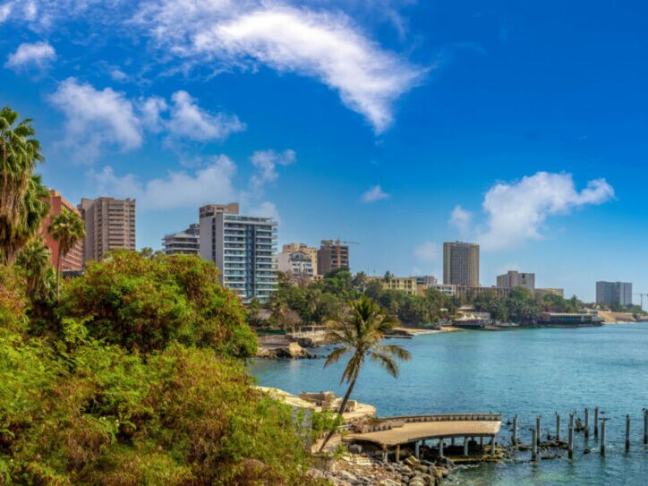 Begrünte Waterfront mit Palmen einer Stadt mit Hochhäusern am Meer.