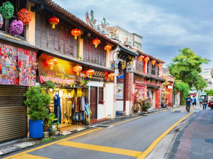Schmale Straße mit Geschäften und roten Lampions um den Eingang zu einem chinesischen Tempel.