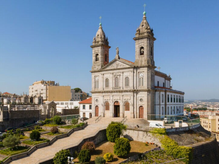 Kirche mit Zwillingstürmen auf einem Hügel über den Dächern einer südländischen Großstadt unter blauem Himmel.