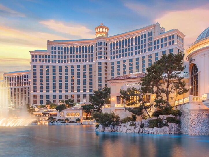 Prunkvoller Hotelkomplex hinter einem künstlichem See mit beleuchteter Wasserfontäne bei Sonnenuntergang.
