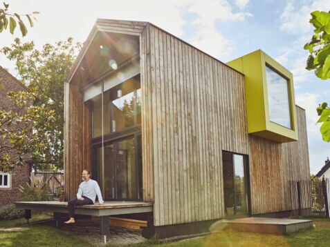 Ein Mann sitzt auf der Terrasse eines Tiny Houses