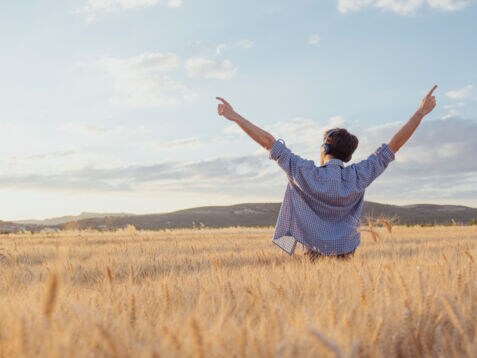 Rückenansicht eines Mannes, der mit ausgestreckten Armen in einem Feld steht.