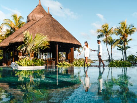 Ein Paar steht an einem luxuriösen Hotelpool am Meer in tropischer Umgebung.