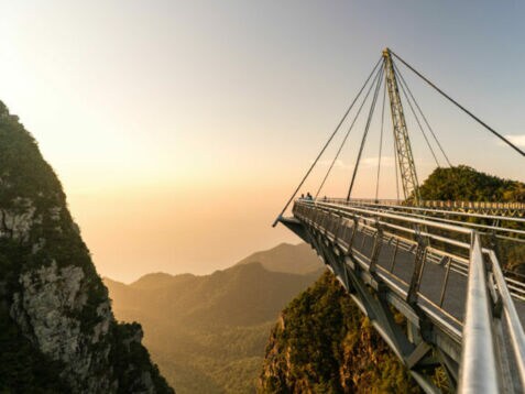 Hängende Fußgängerbrücke mit Stahlseilen über bewaldete Berge bei Sonnenuntergang auf Langkawi.