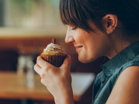Eine Frau hält sich einen Nuss-Muffin an die Nase und lächelt, ihre Augen sind geschlossen.