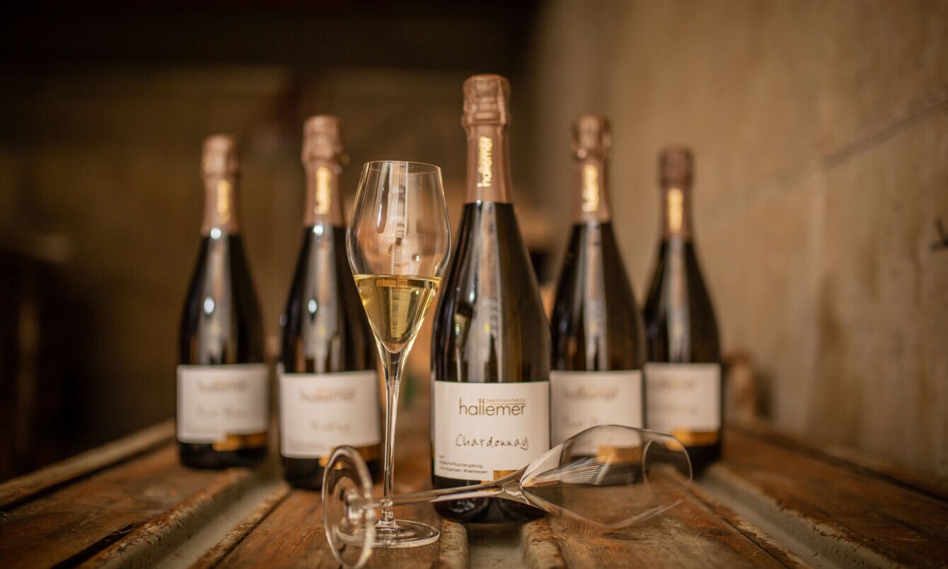 Fünf Winzersektflaschen mit zwei Gläsern in einem rustikalen Ambiente 