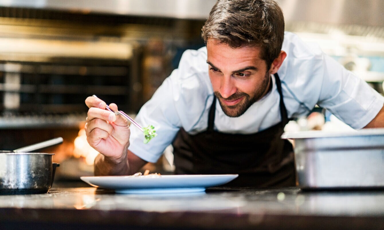 Ein Mann garniert ein Gericht auf einem weißen Teller in einer Restaurantküche.