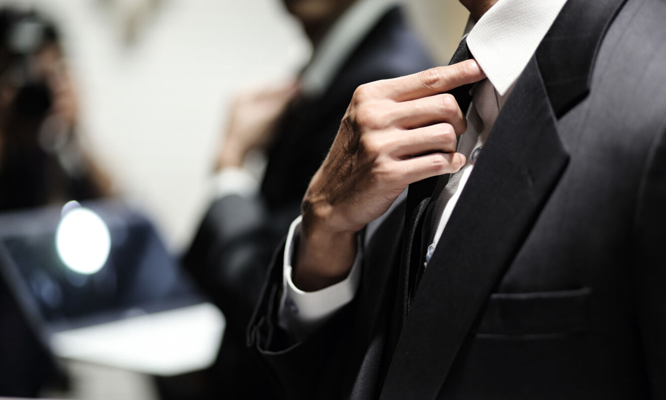 Nahaufnahme eines Mannes im Business-Anzug, der den Sitz seiner Krawatte korrigiert. 
