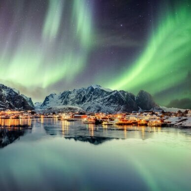 Schneebedeckte Berge und Wasser, darüber grün leuchtende Polarlichter