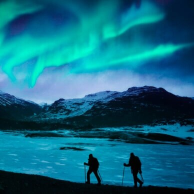 Zwei Wanderer vor einer Bergkulisse mit Polarlichtern.