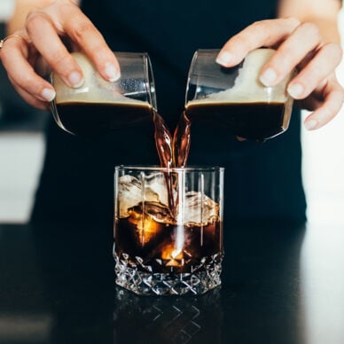 Eine Frau gießt kalten Kaffee in ein Glas mit Eiswürfeln