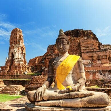 Eine Buddhastatue vor Ruinen eines Tempels