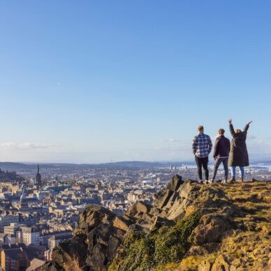 Drei Personen stehen auf einer Erhöhung und blicken von dort über Edinburgh