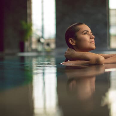 Eine junge Frau entspannt am Beckenrand eines Pools in einem Wellnessbereich.