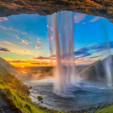 Wasserfall, der von einer Höhle aus bei Sonnenuntergang in eine grüne Landschaft fällt