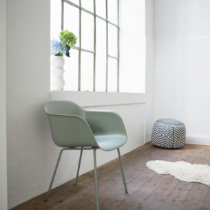 Ein grüner Stuhl aus Plastik steht an einer Wand neben einem Fenster