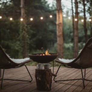 Zwei Stühle auf einem Holzdeck im Wald mit Feuerstelle