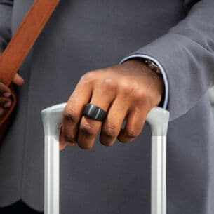 Ein Smart Ring am Mittelfinger einer Hand, die einen Trolley hält
