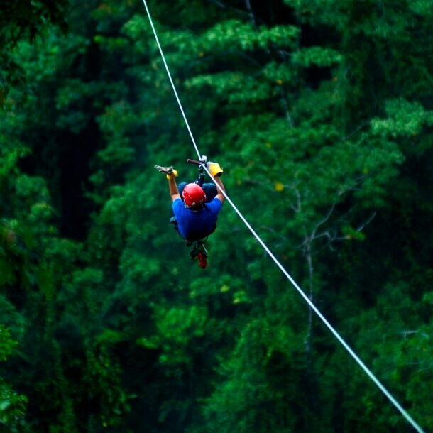 Ein Mann mit Helm gleitet an der Zipline über ein Waldgebiet