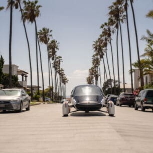 Ein futuristisches Fahrzeug fährt in der Sonne auf palmengesäumter Straße