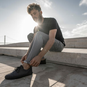 Ein Mann sitzt auf einer Holzpromenade auf einer Steinstufe, die Füße mit schwarzen Sneakern im Vordergrund